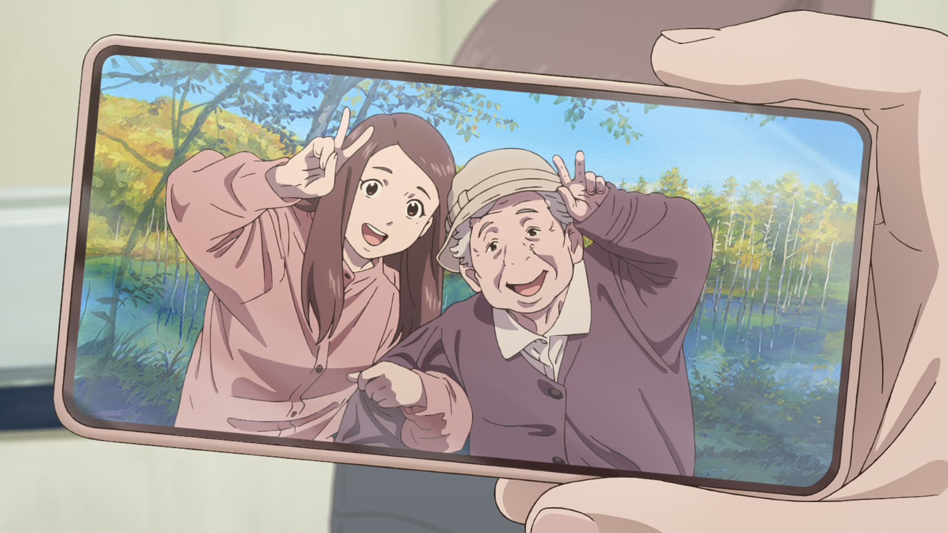 同僚が手にしたまいのスマホ画面 お茶目なポーズで楽しげな祖母との写真が映っている。